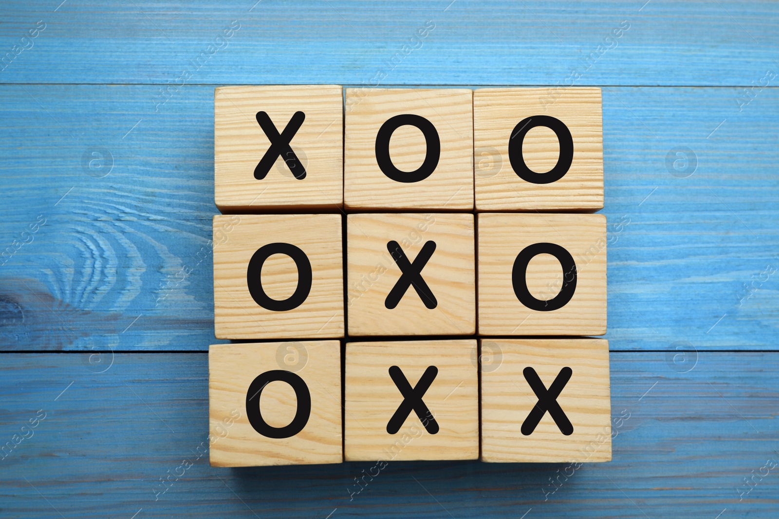 Photo of Tic tac toe cube set on light blue wooden table, flat lay