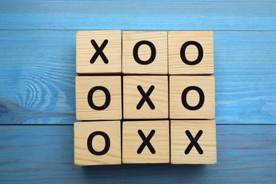 Photo of Tic tac toe cube set on light blue wooden table, flat lay