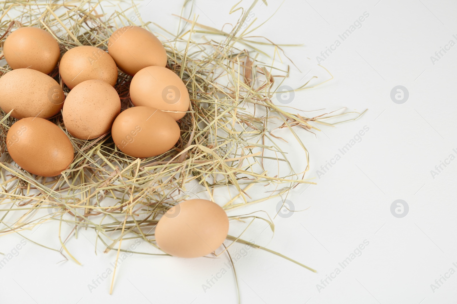 Photo of Raw chicken eggs and decorative straw on white table