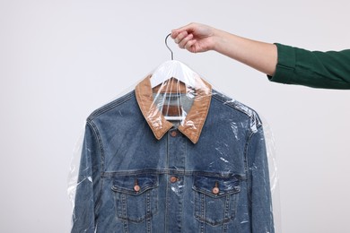 Photo of Dry-cleaning service. Woman holding denim jacket in plastic bag on white background, closeup
