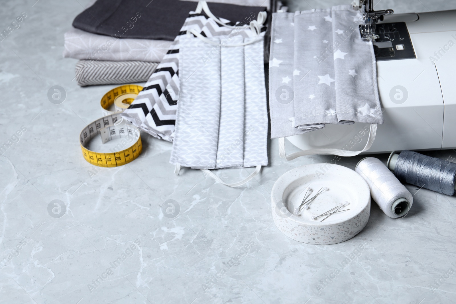 Photo of Sewing machine, homemade protective masks and craft accessories on grey marble table
