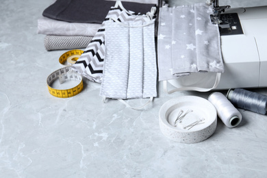 Sewing machine, homemade protective masks and craft accessories on grey marble table