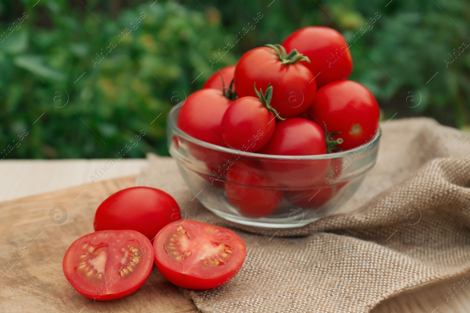 Photo of Bowl with cut and whole red tomatoes on wooden table in garden