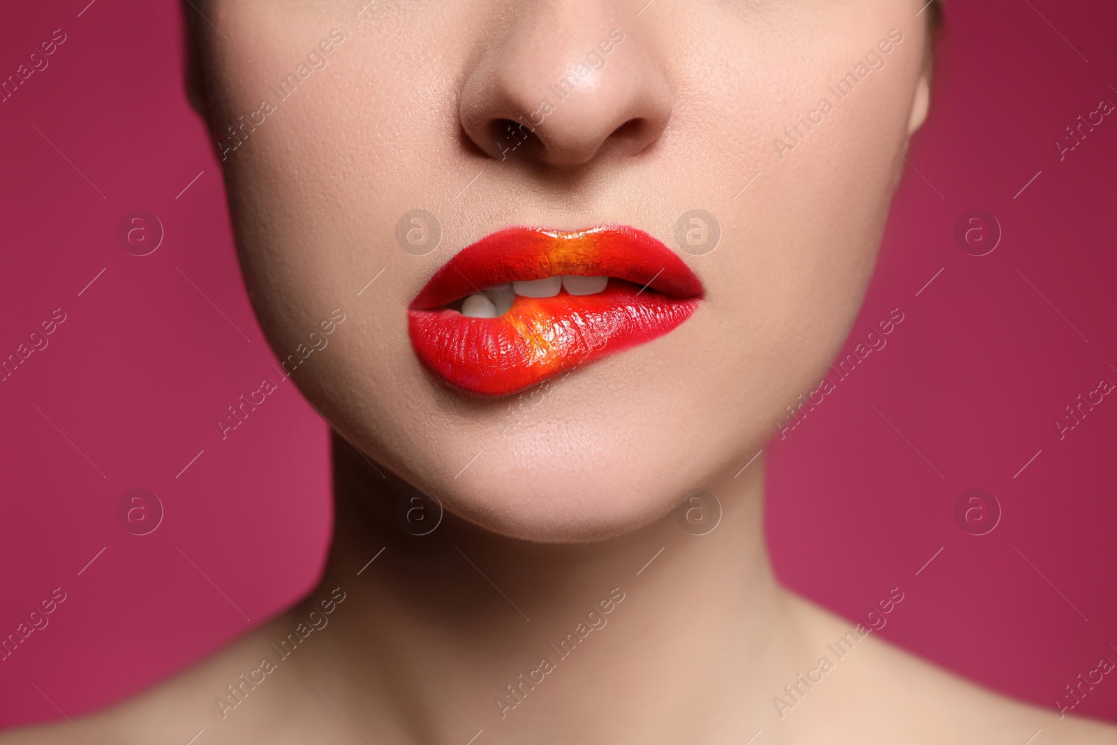 Photo of Young woman with beautiful makeup biting lip on pink background, closeup