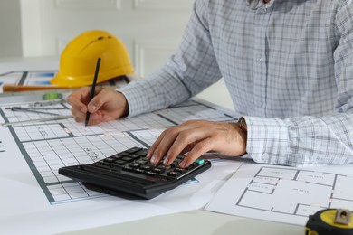 Photo of Architect working with construction drawings and calculator indoors, closeup