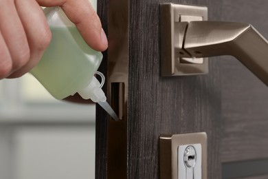 Photo of Handyman lubricating door lock with oil indoors, closeup