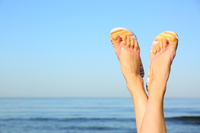 Photo of Closeup of woman wearing flip flops near sea, space for text. Beach accessories