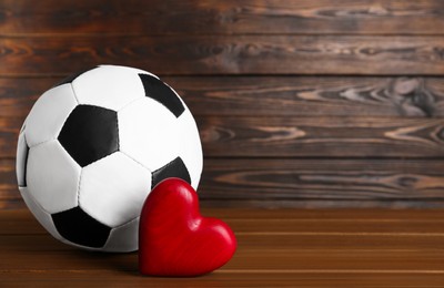 Photo of Soccer ball and heart on wooden table. Space for text