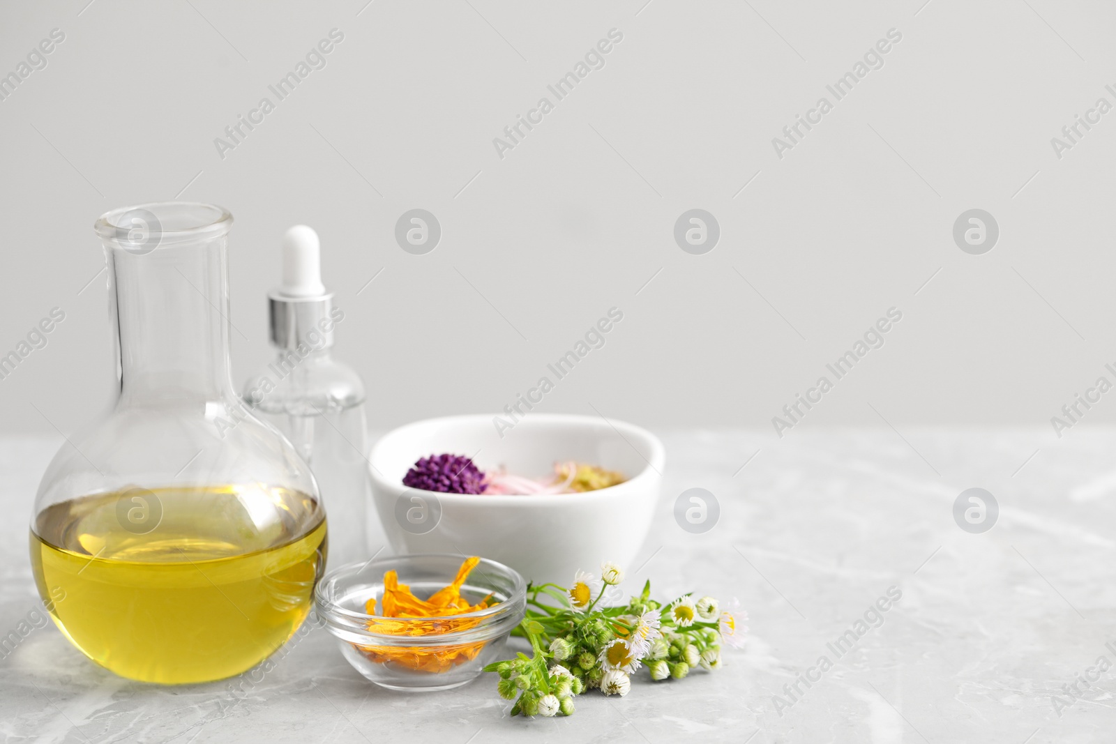 Photo of Cosmetic oil and flowers on light grey table, space for text