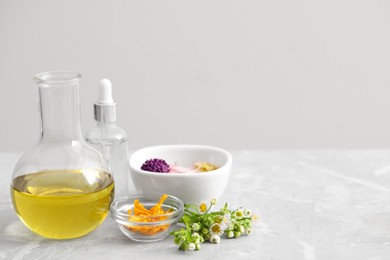 Cosmetic oil and flowers on light grey table, space for text