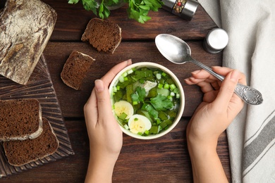 Photo of Woman eating delicious sorrel soup with eggs at wooden table, top view