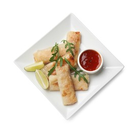 Tasty fried spring rolls, arugula, lime and sauce isolated on white, top view