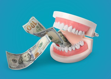 Image of Model of oral cavity with teeth and dollar banknotes on turquoise background. Concept of expensive dental procedures