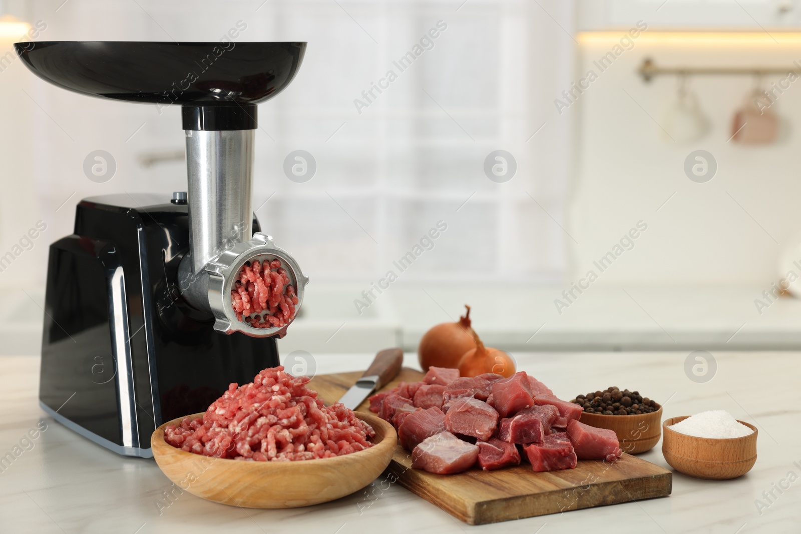 Photo of Electric meat grinder with beef and products on white marble table in kitchen