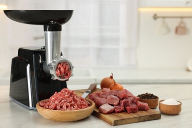 Electric meat grinder with beef and products on white marble table in kitchen