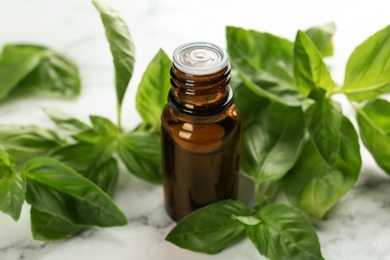 Photo of Bottle of basil essential oil and fresh leaves on marble table