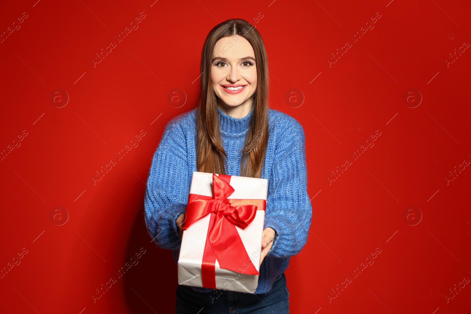 Photo of Young woman in Christmas sweater holding gift box on red background