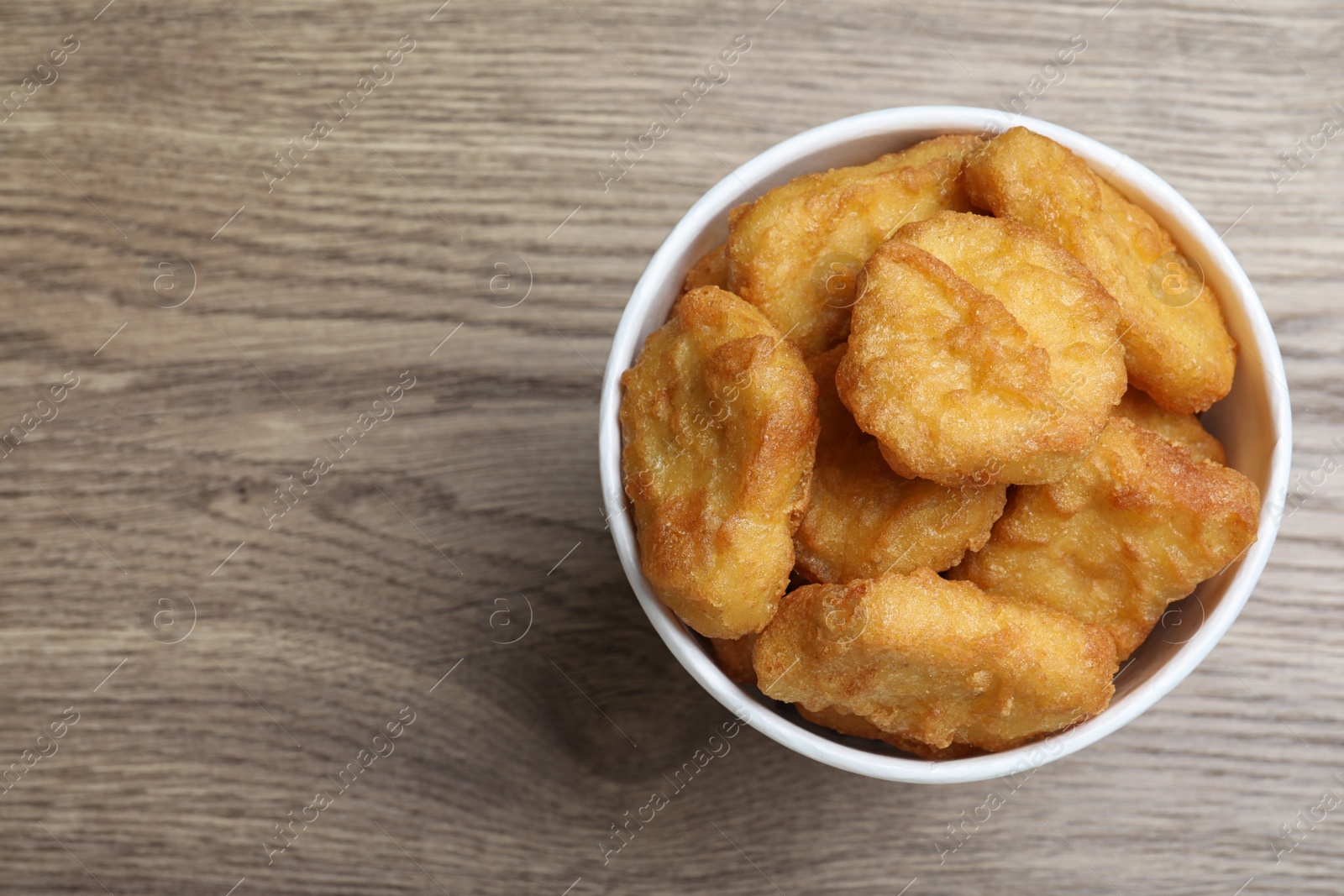 Photo of Bucket with tasty chicken nuggets on wooden table, top view. Space for text