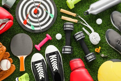 Photo of Different sport equipment and sneakers on green grass, flat lay