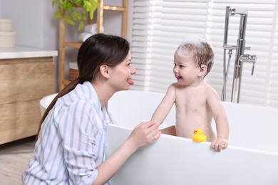 Photo of Mother bathing her cute little baby in tub at home