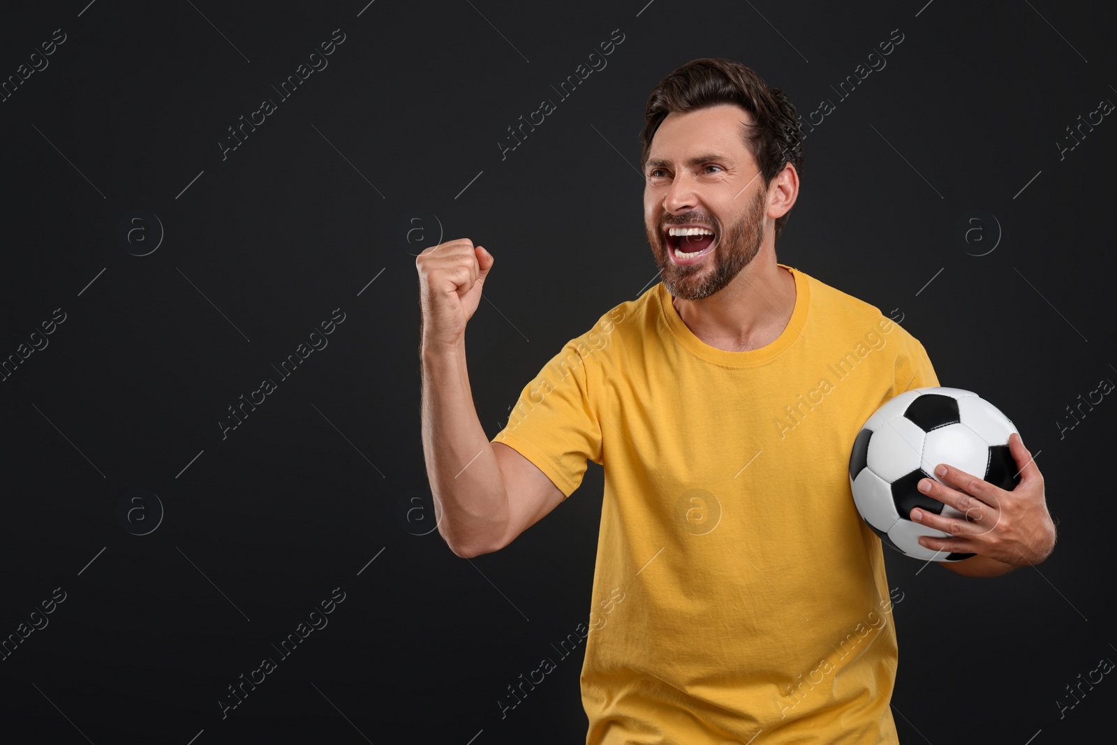 Photo of Emotional sports fan with soccer ball on black background, space for text