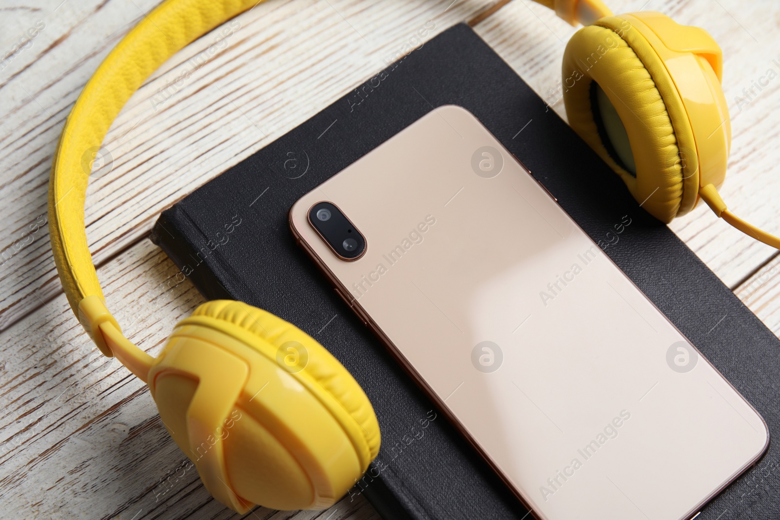 Photo of Book, modern headphones and smartphone on white wooden table, closeup