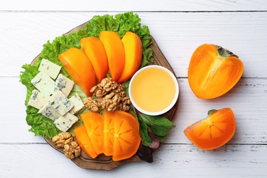 Photo of Delicious persimmon, blue cheese, nuts and honey served on white wooden table, flat lay