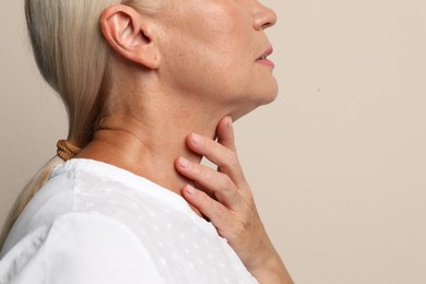 Mature woman doing thyroid self examination on beige background closeup