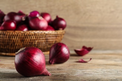 Photo of Fresh red onion bulbs on wooden table, space for text