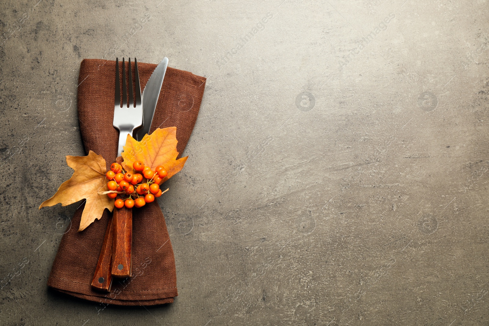 Photo of Top view of cutlery with napkin, ashberries and autumn leaves on grey table, space for text. Thanksgiving Day