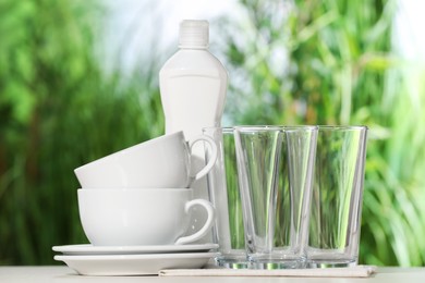 Set of clean dishware and detergent on white table against blurred background