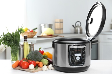 Modern multi cooker and products on table in kitchen. Space for text