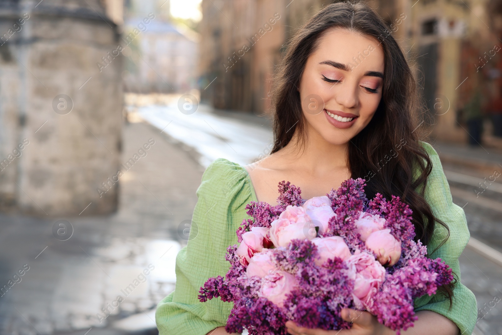 Photo of Beautiful woman with bouquet of spring flowers on city street, space for text