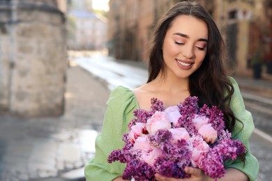 Beautiful woman with bouquet of spring flowers on city street, space for text