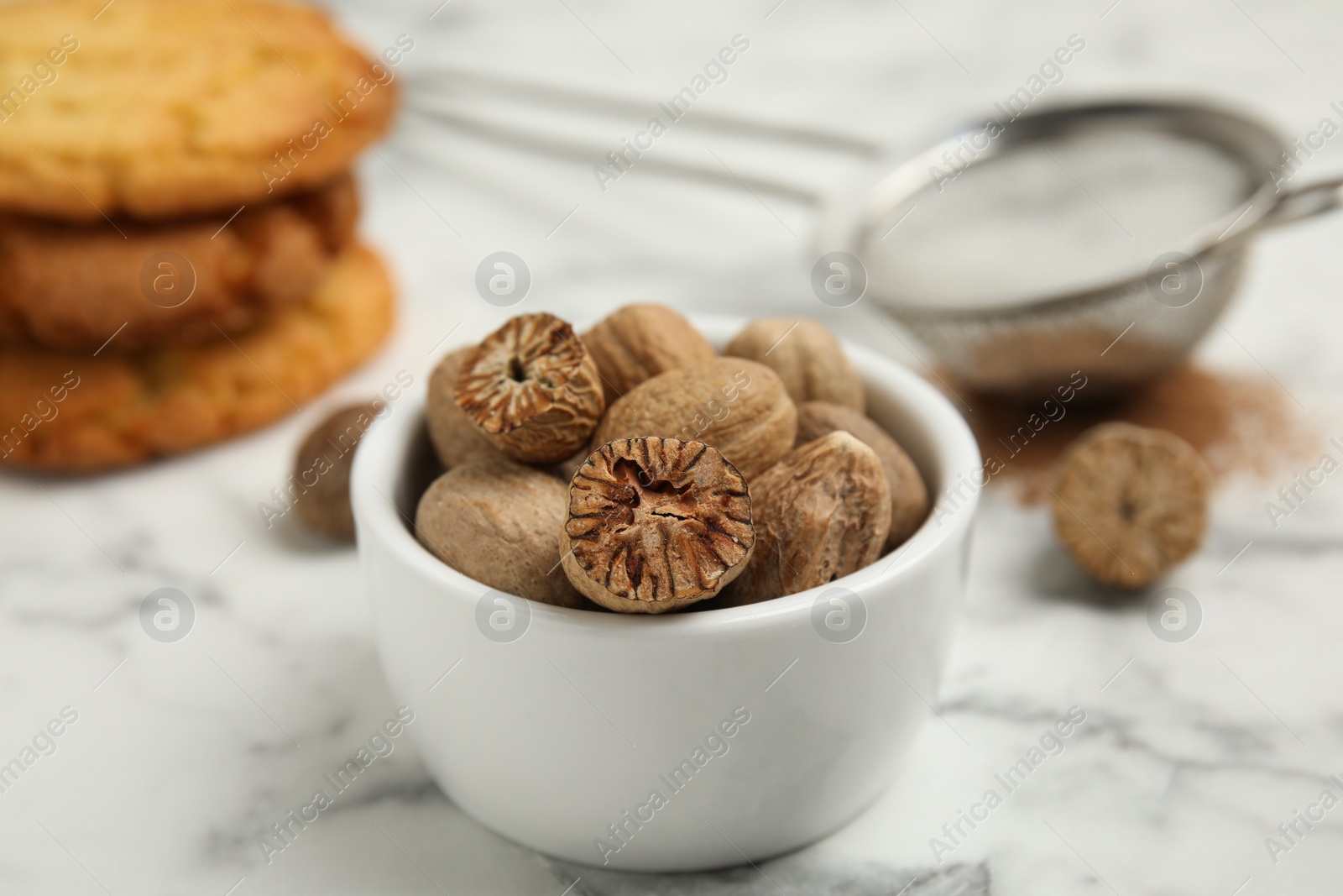 Photo of Nutmeg seeds in bowl on white marble table, closeup