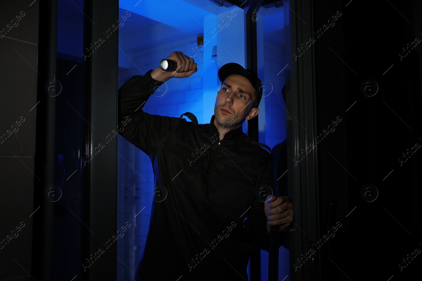 Photo of Male security guard with flashlight near entrance door at night