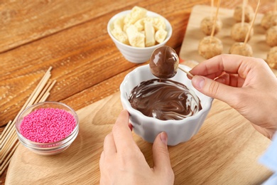 Young woman with cake pop in chocolate frosting at wooden table, closeup