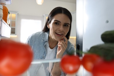 Photo of Thoughtful woman near refrigerator in kitchen, view from inside