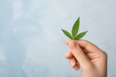 Photo of Woman holding hemp leaf on light blue background, closeup. Space for text