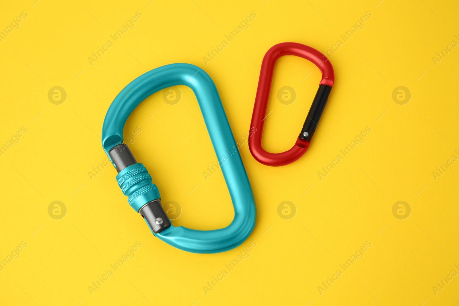 Photo of Two metal carabiners on yellow background, above view