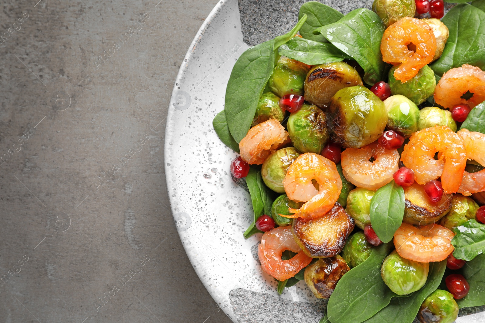 Photo of Plate of warm salad with Brussels sprouts on grey table, top view. Space for text