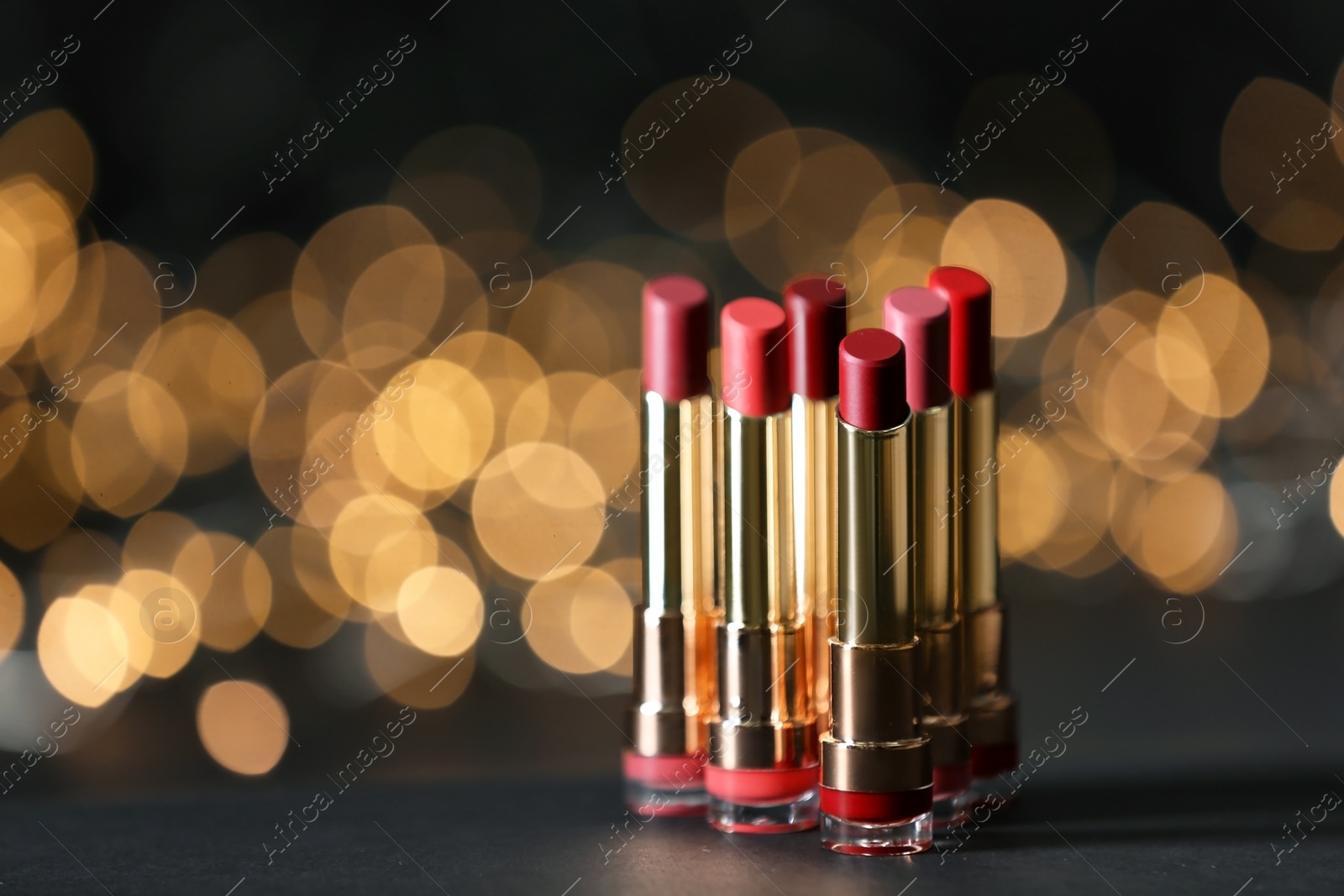 Photo of Set of bright lipsticks on table against blurred lights, space for text