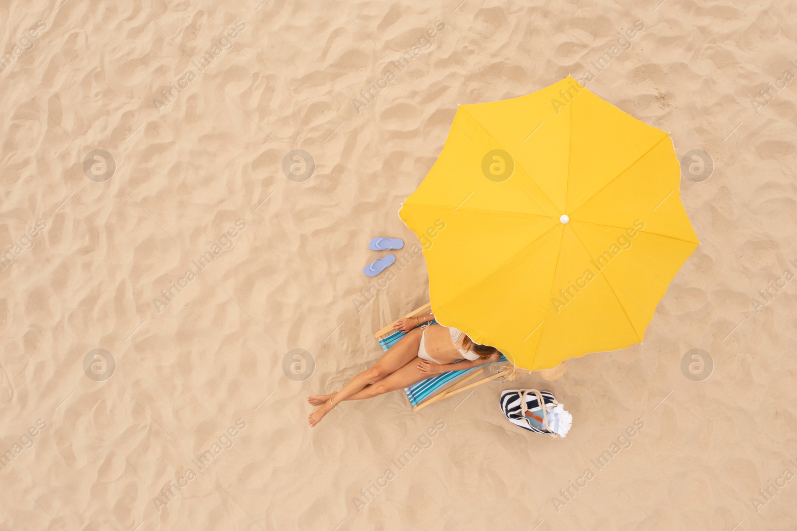 Image of Woman resting in sunbed under yellow beach umbrella at sandy coast, aerial view. Space for text