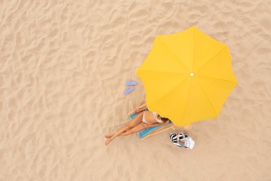 Image of Woman resting in sunbed under yellow beach umbrella at sandy coast, aerial view. Space for text