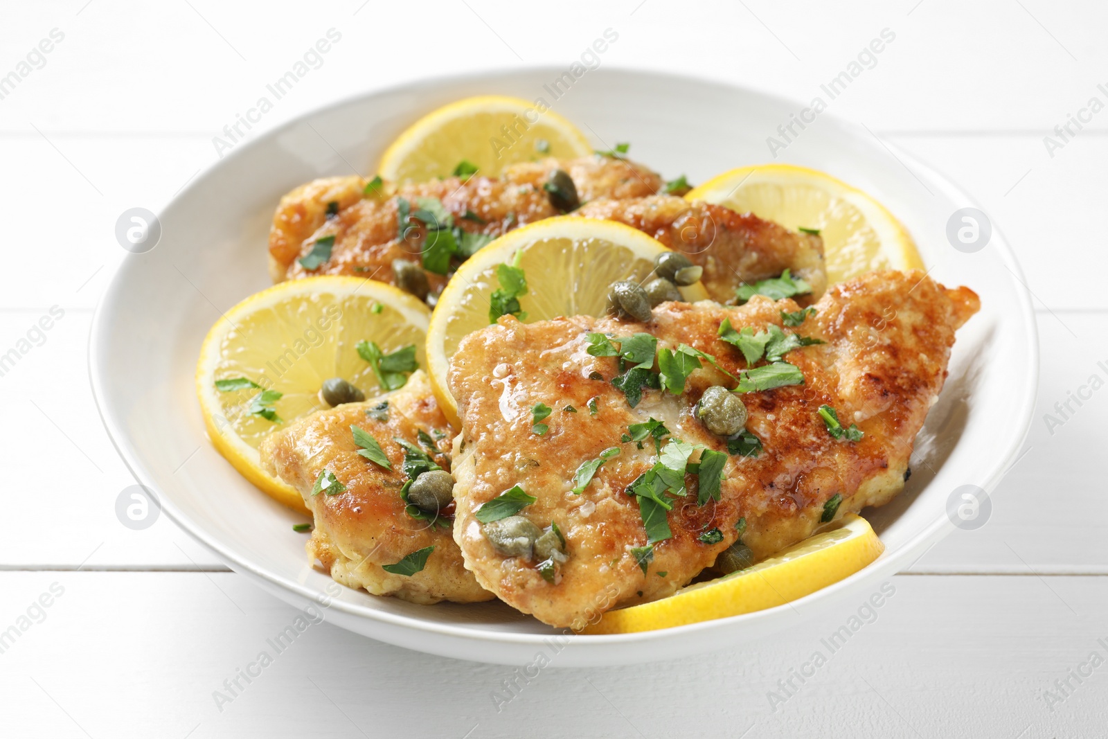 Photo of Delicious chicken piccata on white wooden table