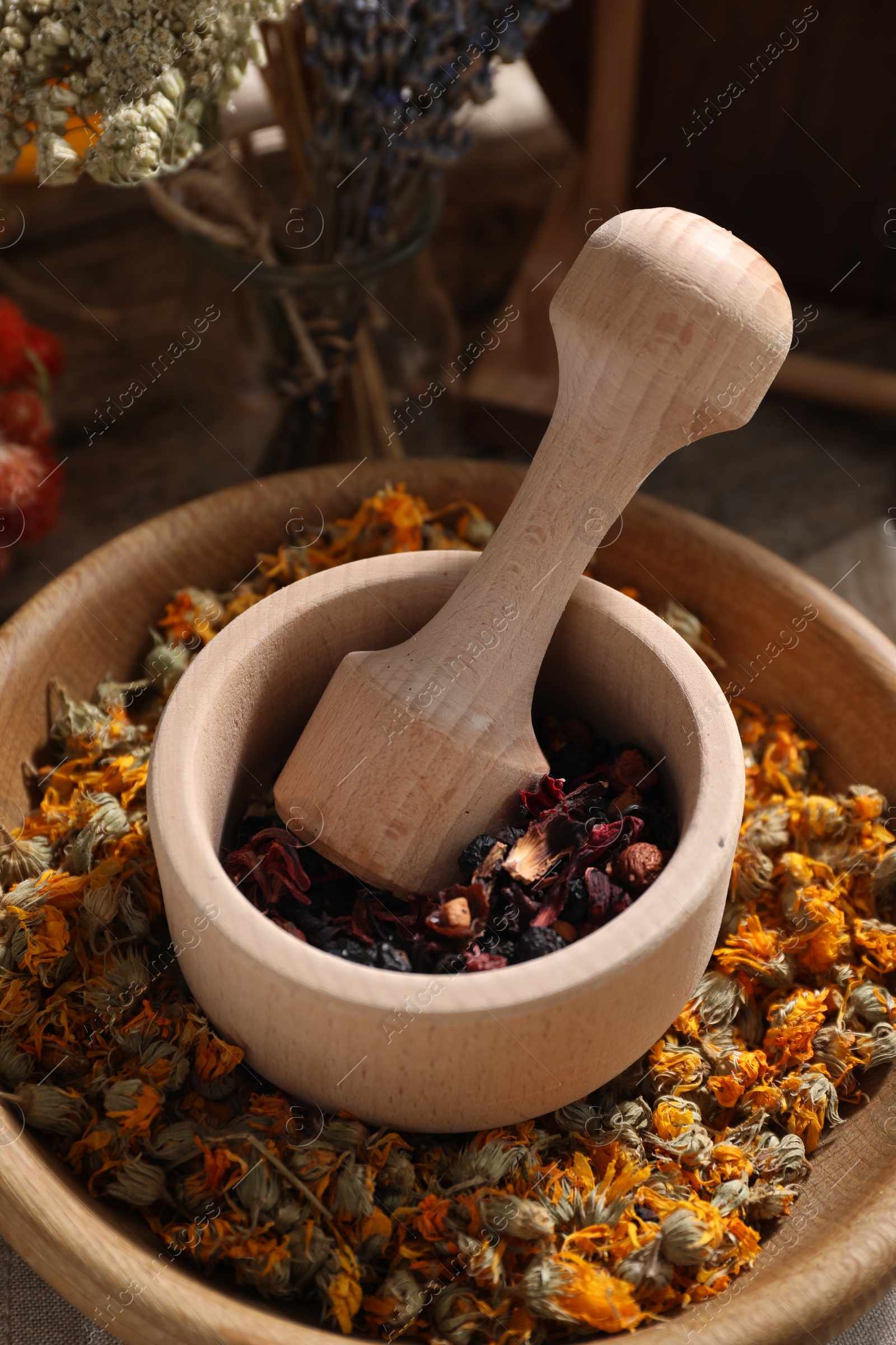 Photo of Mortar with pestle, many different dry herbs and flowers on table, closeup