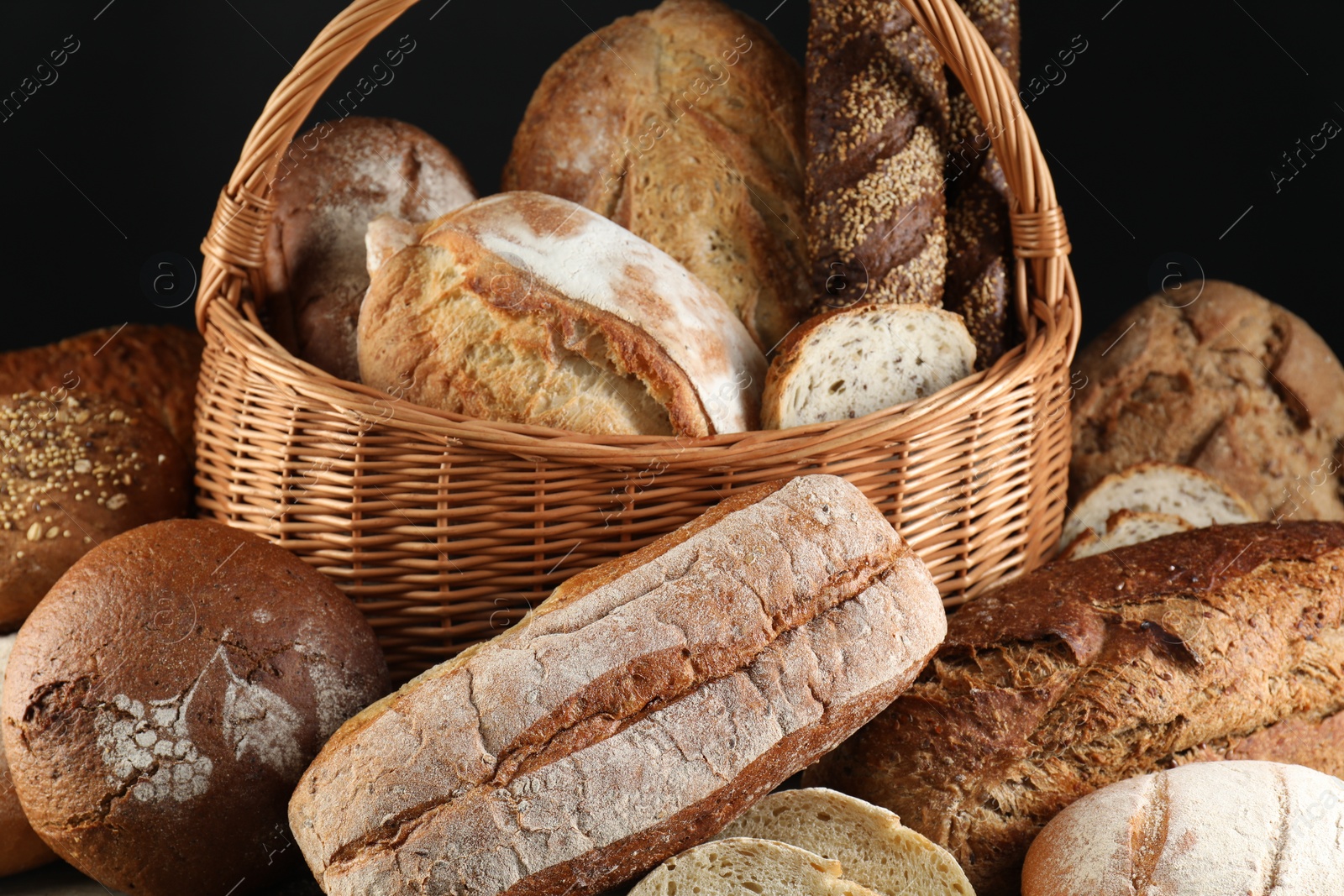 Photo of Wicker basket with different types of fresh bread against black background