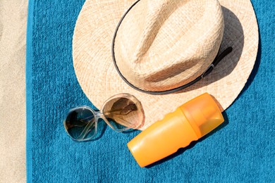 Soft blue beach towel with straw hat. bottle of sunblock and sunglasses on sand, flat lay