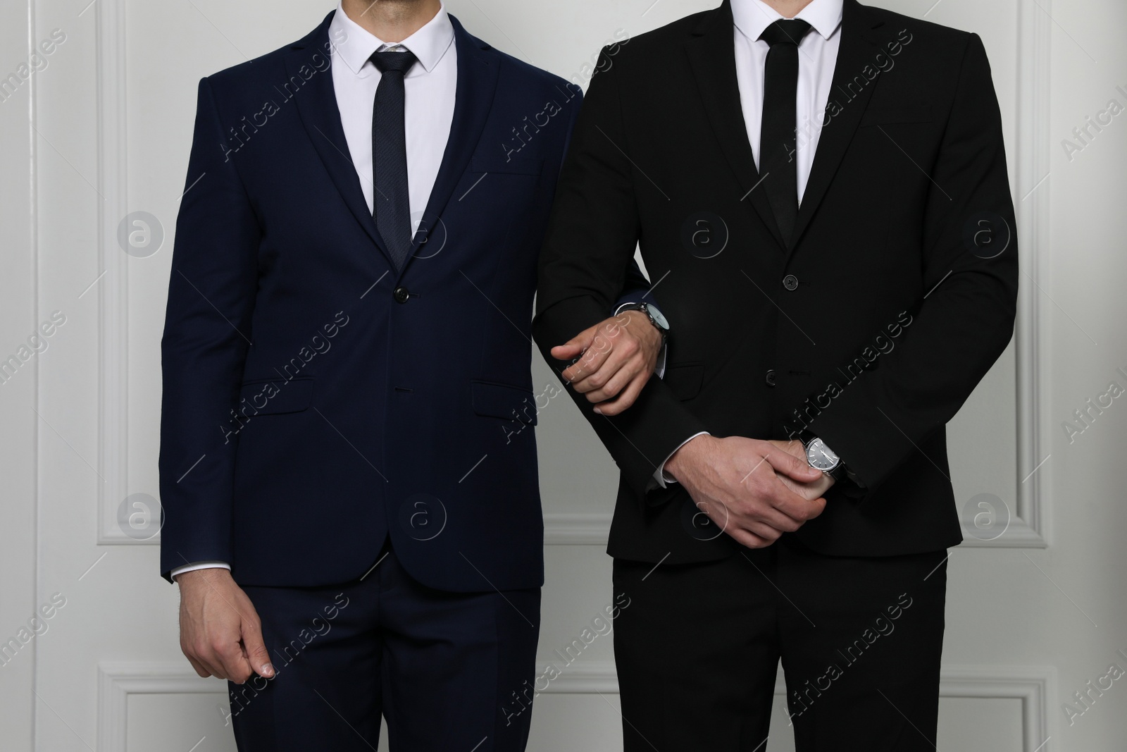 Photo of Gay couple in elegant suits standing near white wall, closeup