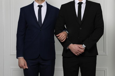 Photo of Gay couple in elegant suits standing near white wall, closeup